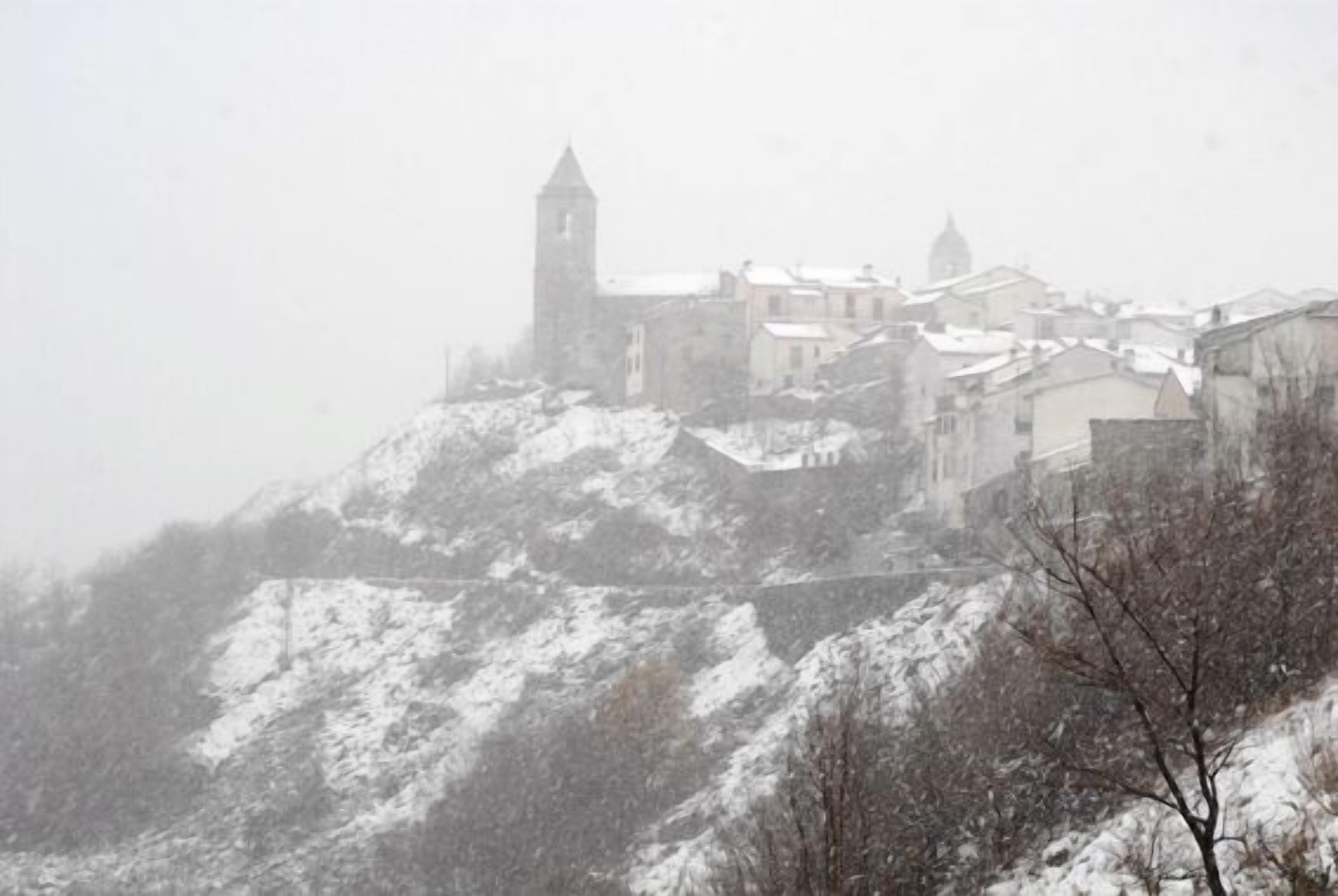 A snow-covered hill with a historic building featuring a tower, surrounded by other buildings.