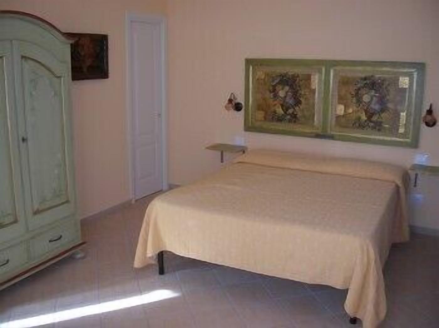 A bedroom with a bed, a wardrobe, and two framed artworks on the wall.