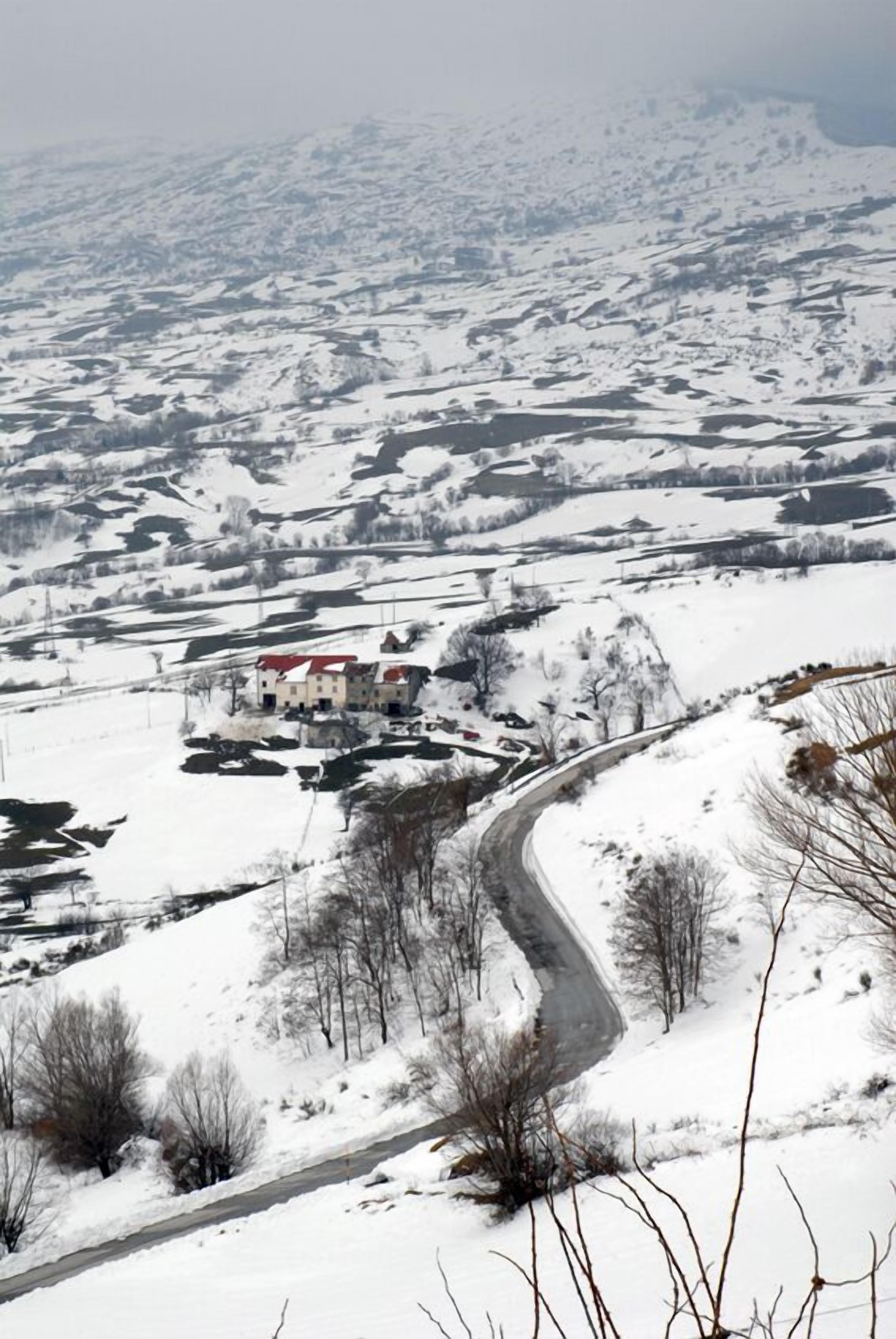 Eine verschneite Landschaft mit einer kurvenreichen Straße und einem Gebäude mit rotem Dach.