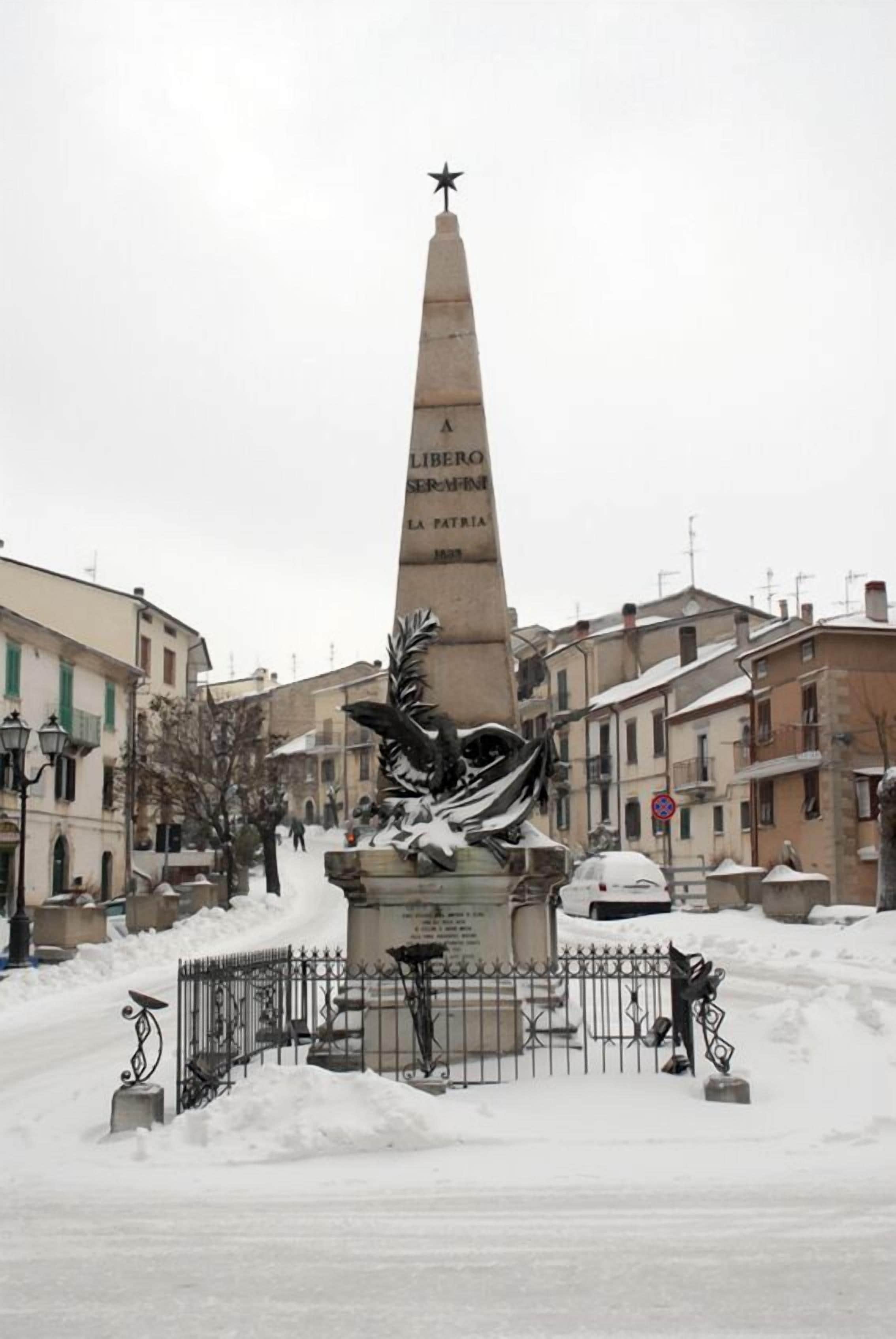 Un monument orné d’inscriptions et doté d’une base décorative, entouré de neige et de bâtiments.