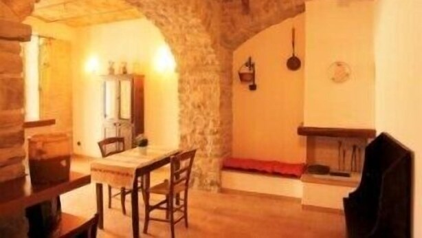 Un comedor con un arco de piedra, una mesa de madera, sillas y una lámpara colgante.