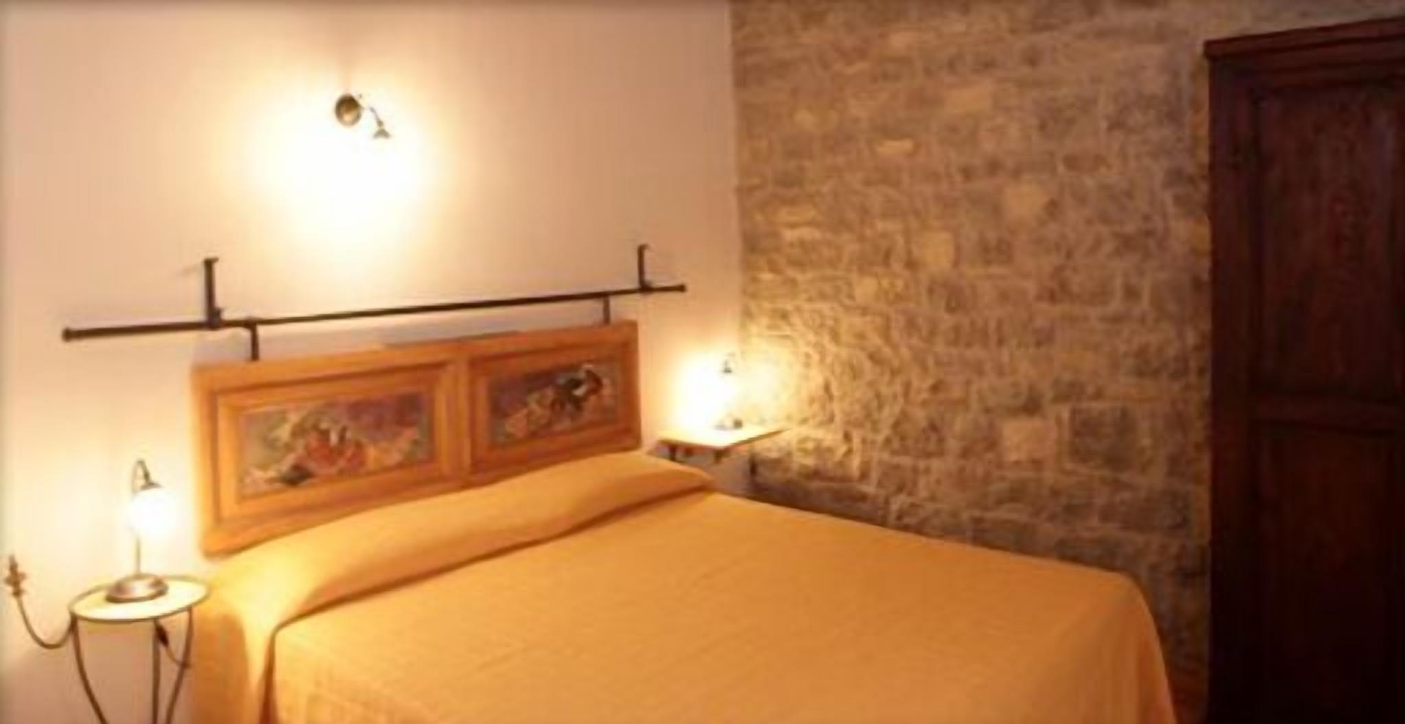 Een bed met hoofdbord, twee wandlampen en een stenen muur.