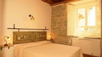 A bedroom with a wooden headboard, a bed with a white bedspread, two bedside lamps, a stone wall, and a window with a view of the outside.