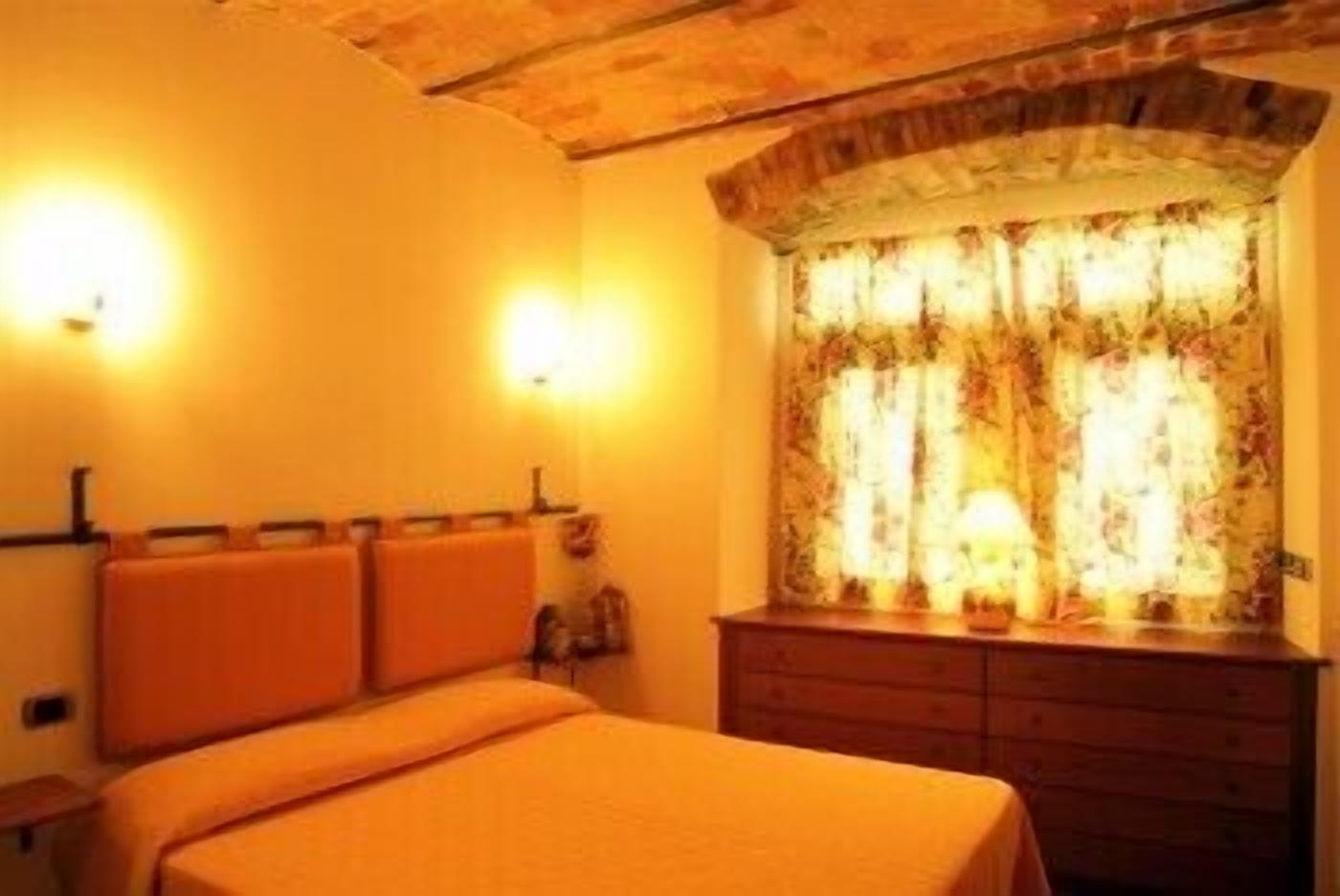 Une chambre d’hôtel avec un lit, une commode en bois et une fenêtre ornée de rideaux à motifs floraux.