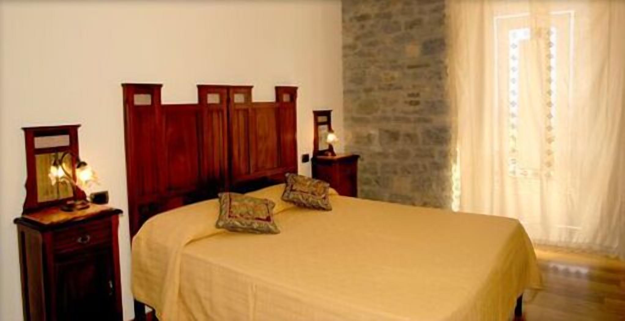 A bedroom with a wooden headboard, two bedside tables with lamps, a bed with a beige bedspread, and a stone wall.