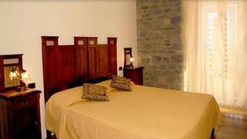 A bedroom with a wooden headboard, two bedside tables with lamps, a bed with a beige bedspread, and a stone wall.
