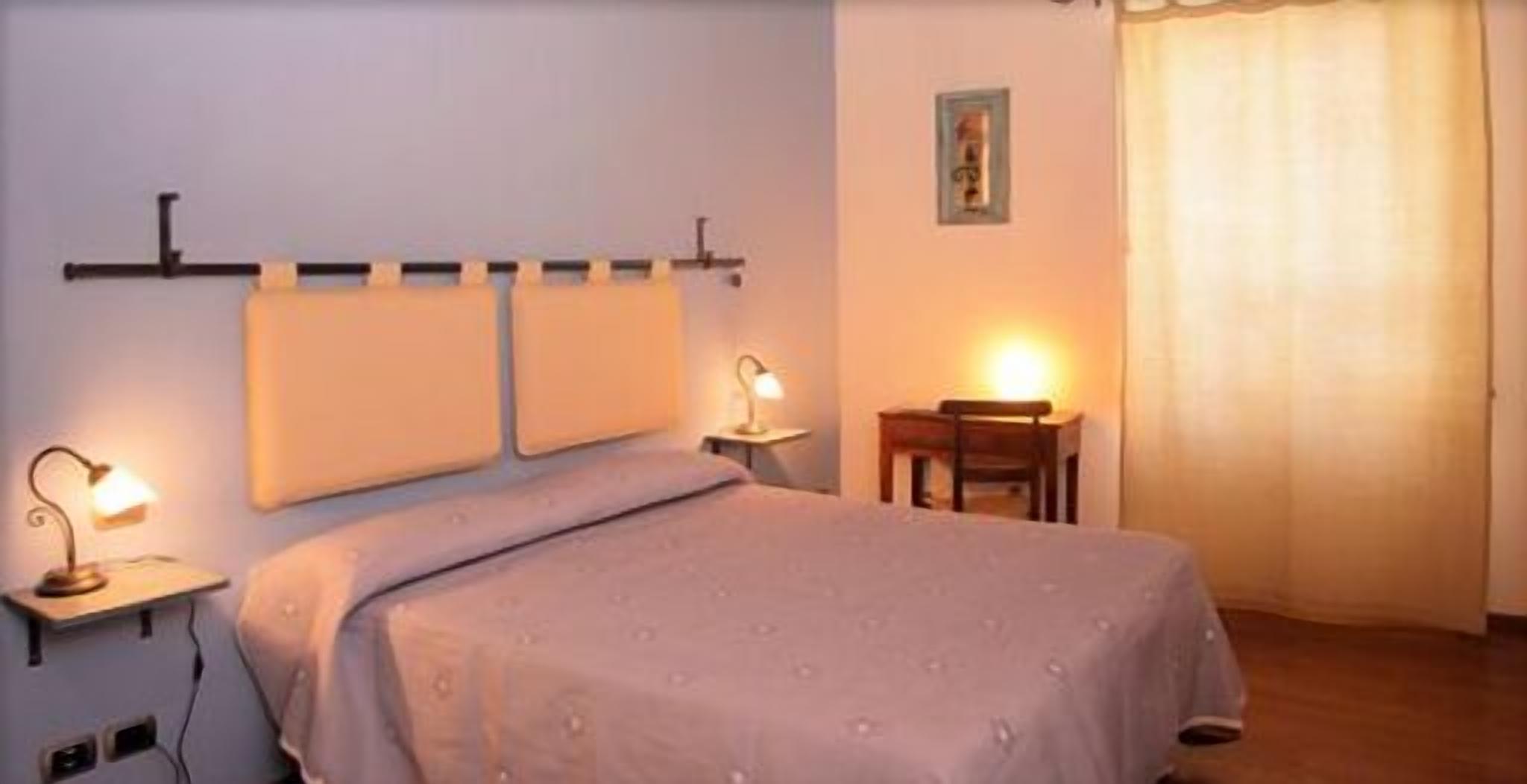 A bedroom with a bed, two bedside tables with lamps, a chair, and a small table.