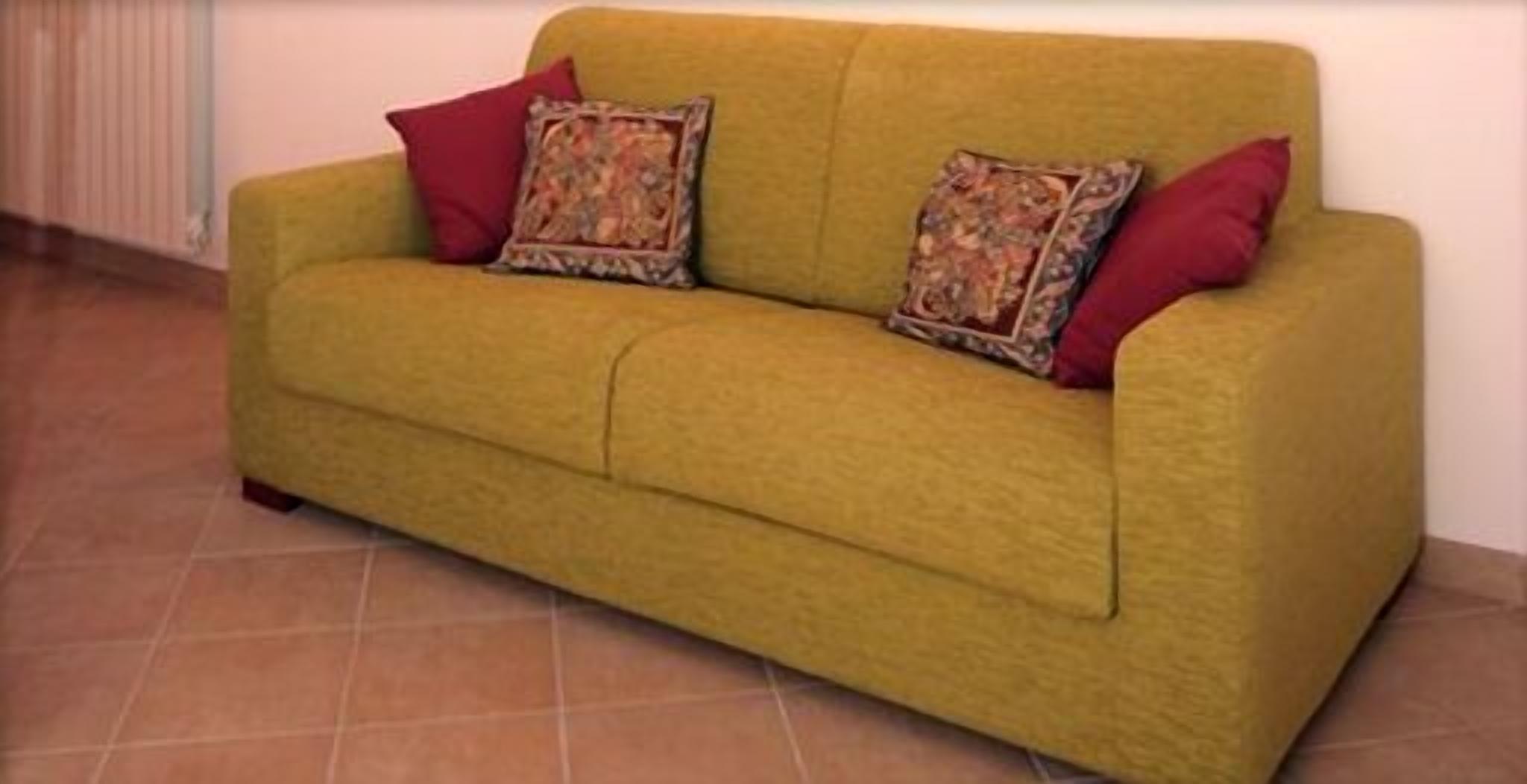 A yellow sofa with two patterned pillows and a red pillow against a plain wall.