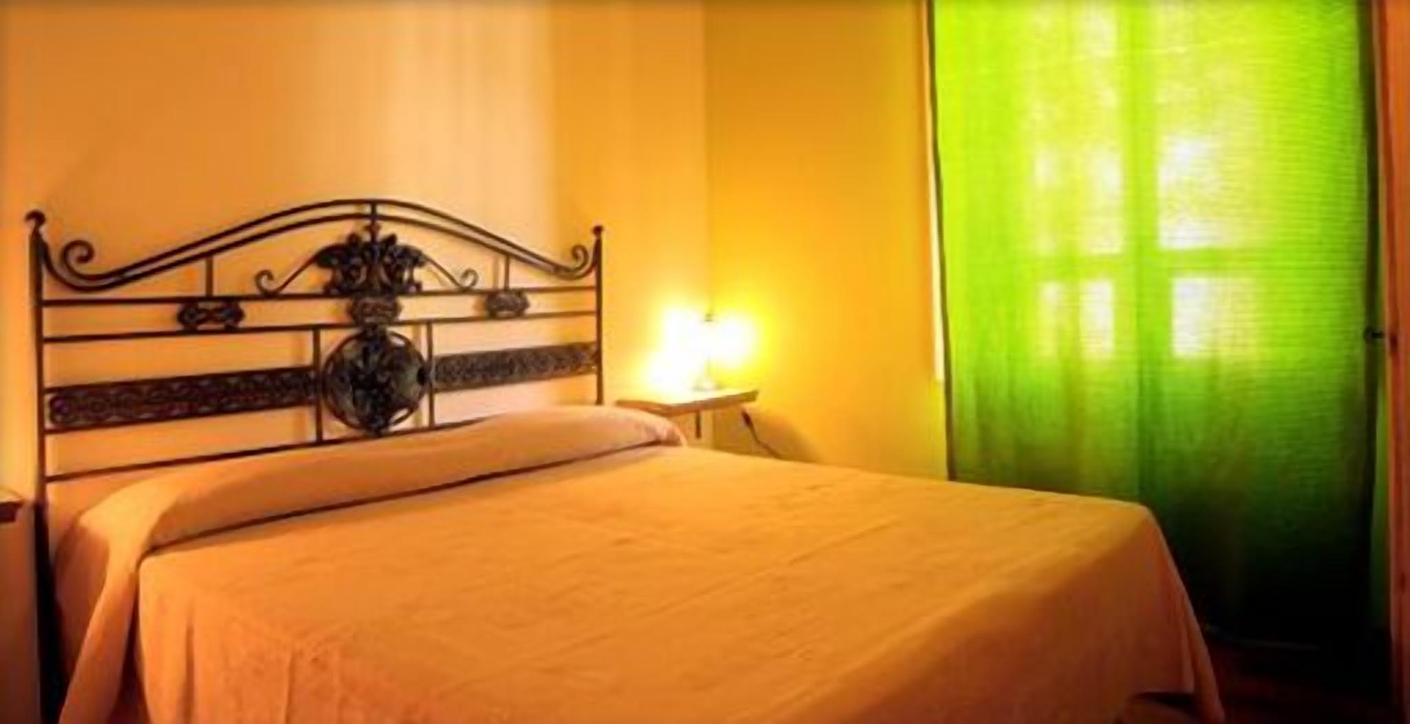A bed with a headboard, a bedside table with a lamp, and a green curtain.