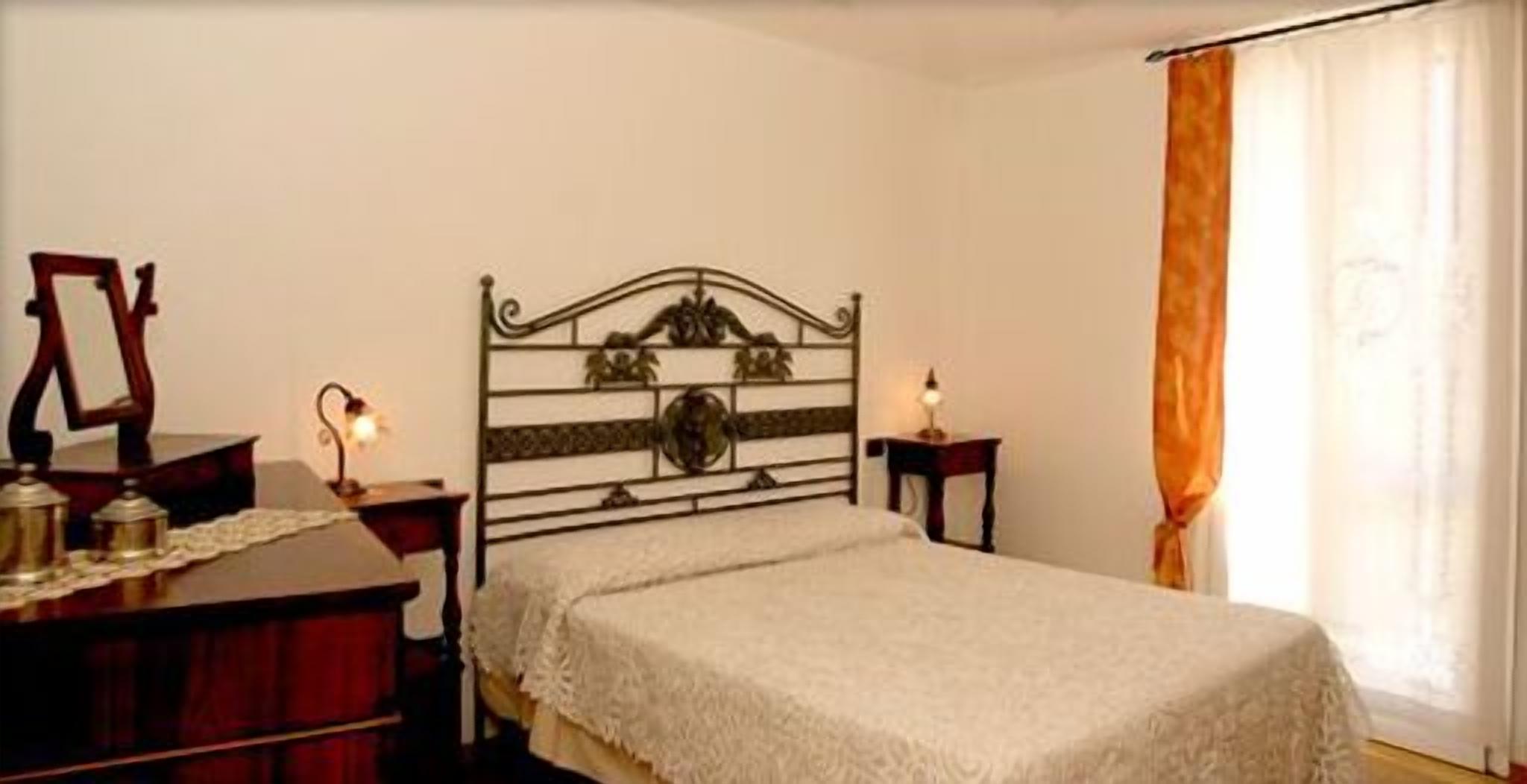 A bedroom with a bed, a dresser, a nightstand, a lamp, and a window with curtains.