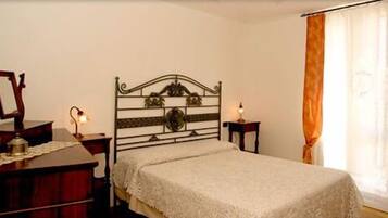 A bedroom with a bed, a dresser, a nightstand, a lamp, and a window with curtains.