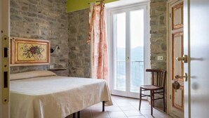 Un dormitorio con cama, una silla, un cuadro y vistas por una puerta.