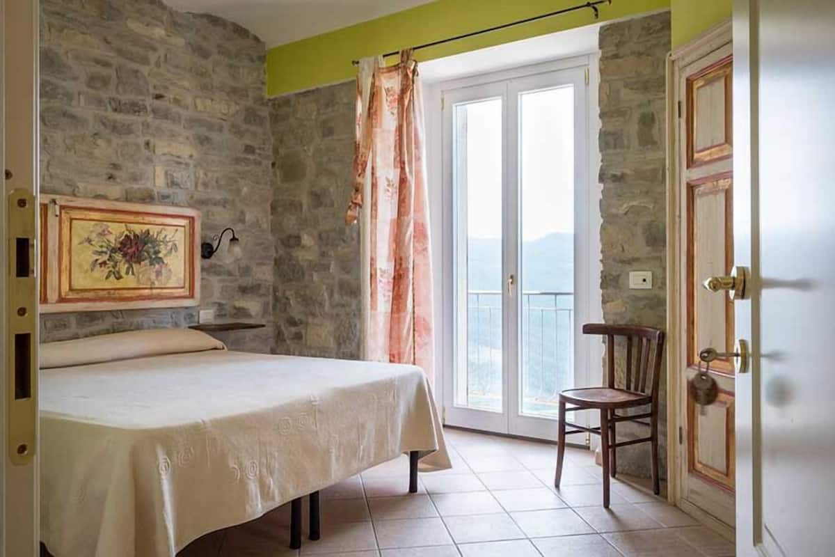 A bedroom with a bed, a chair, a painting, and a view through a door.