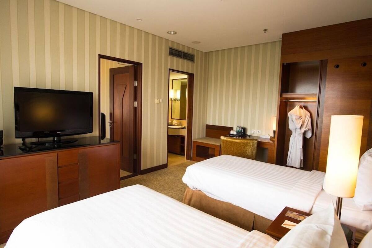 A hotel room with two beds, a television, a mirror, a robe, and a lamp.