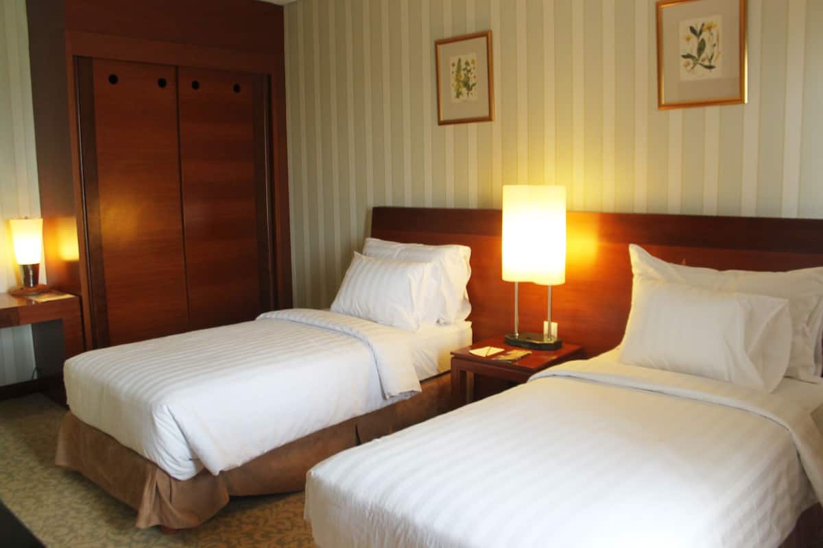 A hotel room with two beds, a wooden wardrobe, and two bedside lamps.