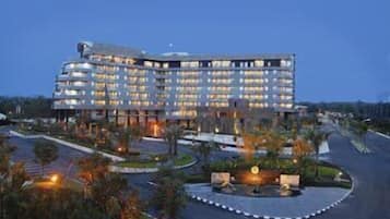 A multi-story hotel with a modern design, featuring a central courtyard and a parking area.