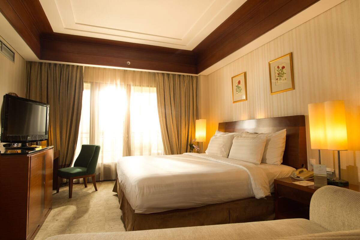 A hotel room with a large bed, a television, a desk with a lamp, and two framed pictures on the wall.