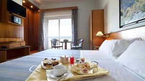 A hotel room with a bed, a breakfast tray with pastries and drinks, a TV, and a painting on the wall. - Giulia Hotel (Camaiore)