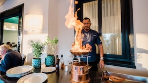 A chef performing a flambé with a copper pot on a table in a restaurant setting. - Giulia Hotel (Camaiore)