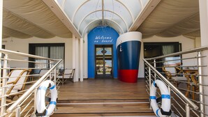 A ship's deck with lifeboats, a blue wall with "Welcome on board" text, and a large cylindrical structure. - Giulia Hotel (Camaiore)