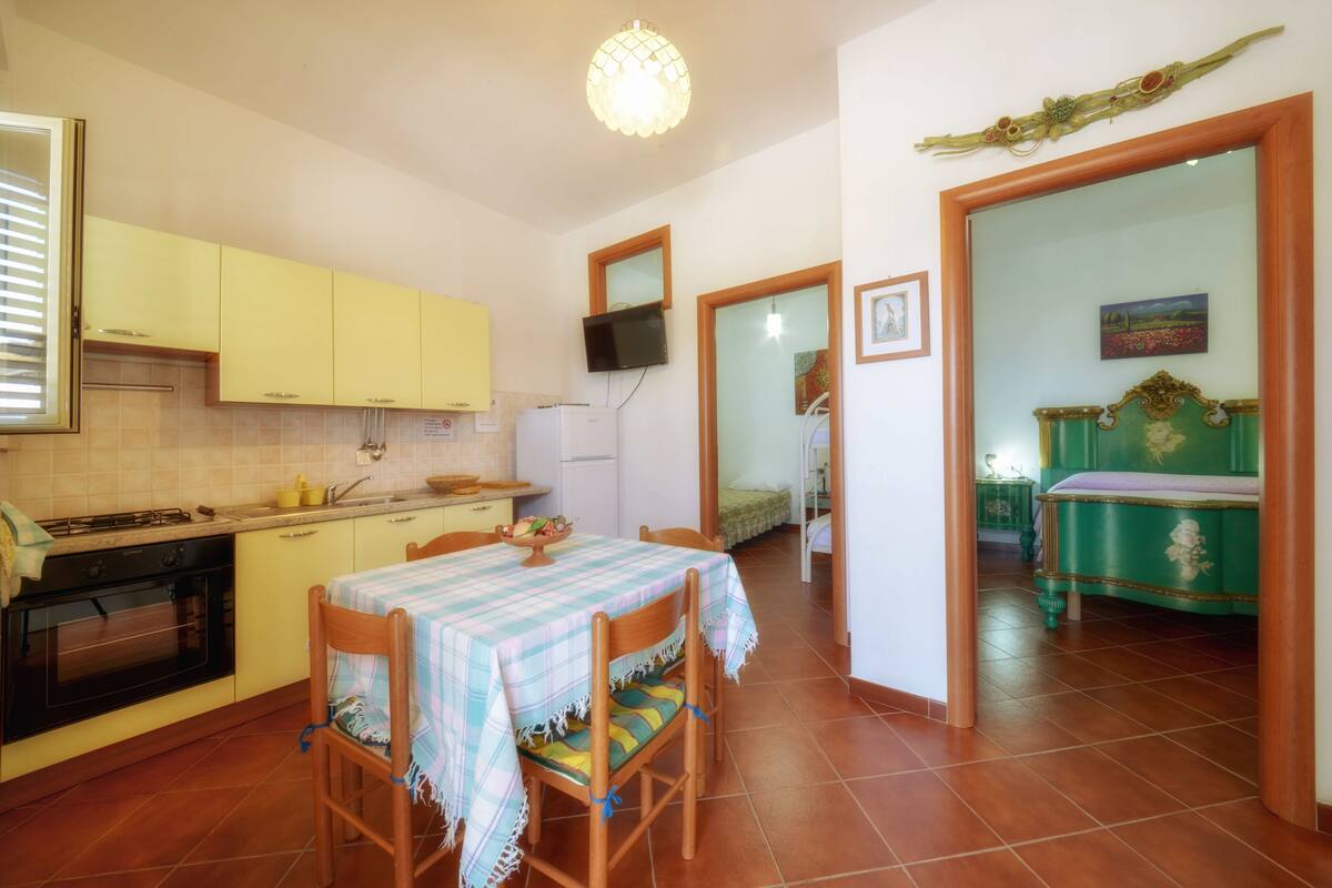 A compact kitchen with yellow cabinets, a dining table with a checkered tablecloth, and a television mounted on the wall.