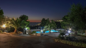 A nighttime view of a resort with a swimming pool, stone walls, and palm trees. - B&B Villa Nicoletta (Peschici)