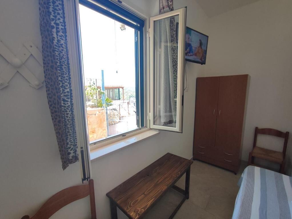 A room with a window, a bench, a wardrobe, and a bed.