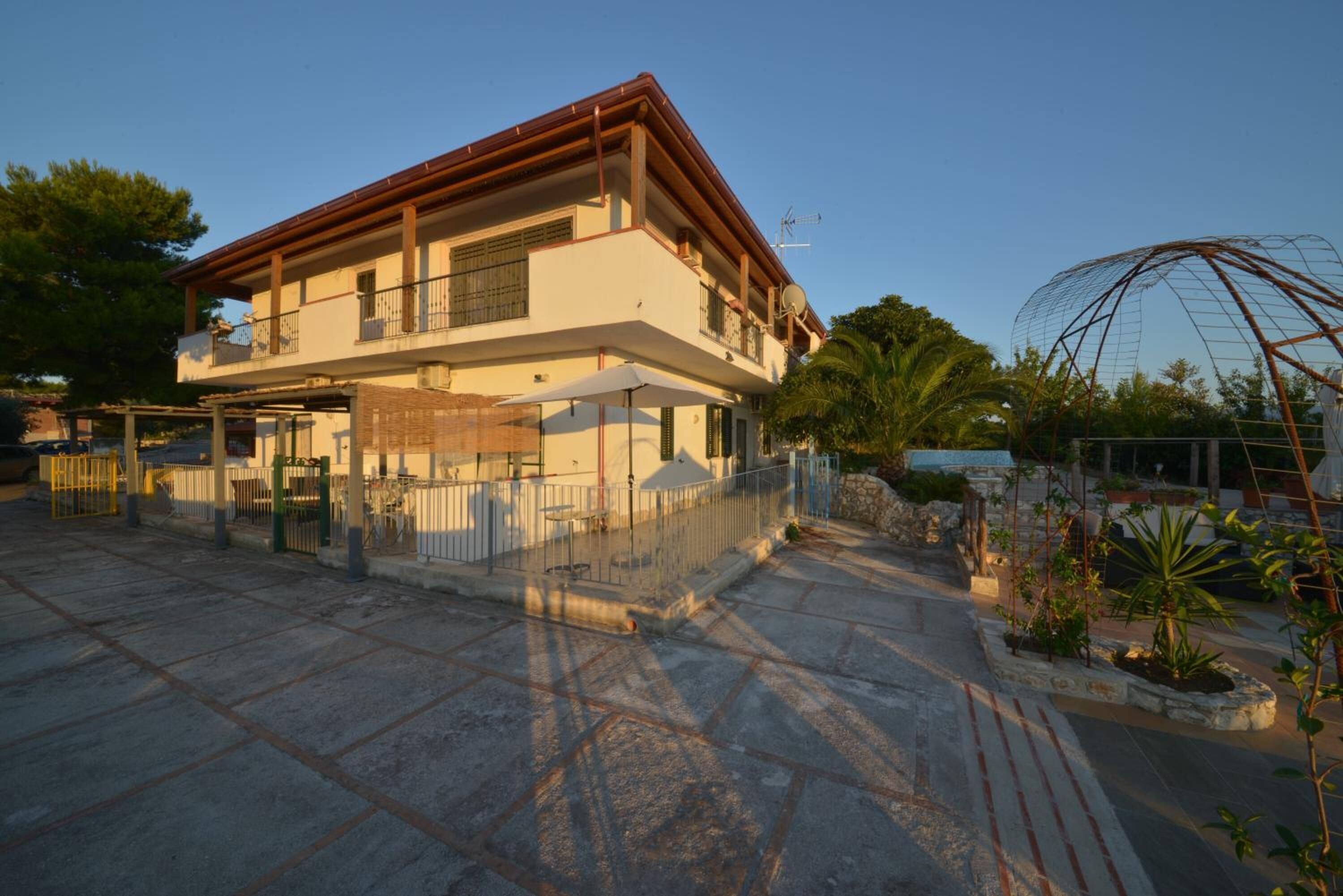 Una casa de dos pisos con un balcón, un espacio exterior cubierto y un jardín vallado.