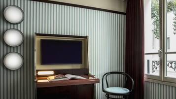 A room with a television, a desk with a book, a chair, and a window with a view of the outside.