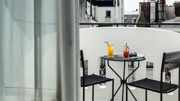 En balkon med et bord og to stole, to drikkevarer på bordet, og udsigt til bygninger i baggrunden.