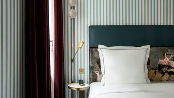 Une chambre d’hôtel avec un papier peint à rayures, une tête de lit sombre, une table de chevet avec une lampe et un tableau au mur.