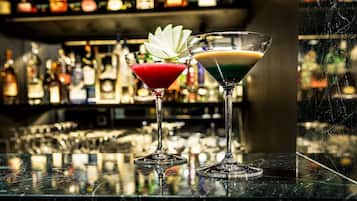 Dos copas de martini sobre una barra con un fondo desenfocado de diversas botellas.
