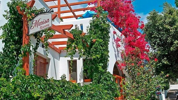 Un edificio con un letrero que dice "Marina Rooms", con fachada blanca, vigas de madera rojas y abundante vegetación.
