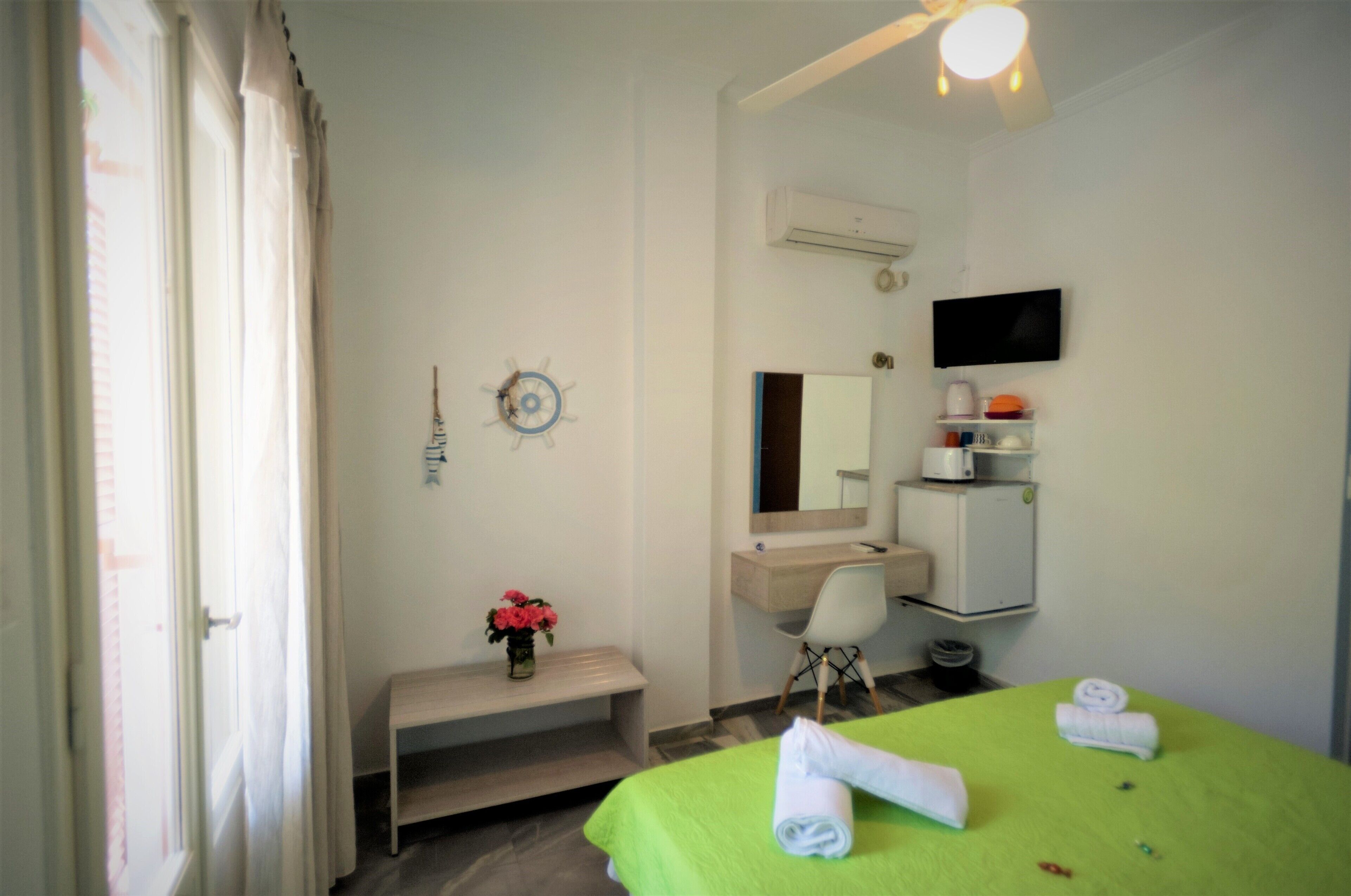 A hotel room with a bed, a desk, a chair, a vanity with a mirror, a small shelf with toiletries, and a wall-mounted TV.