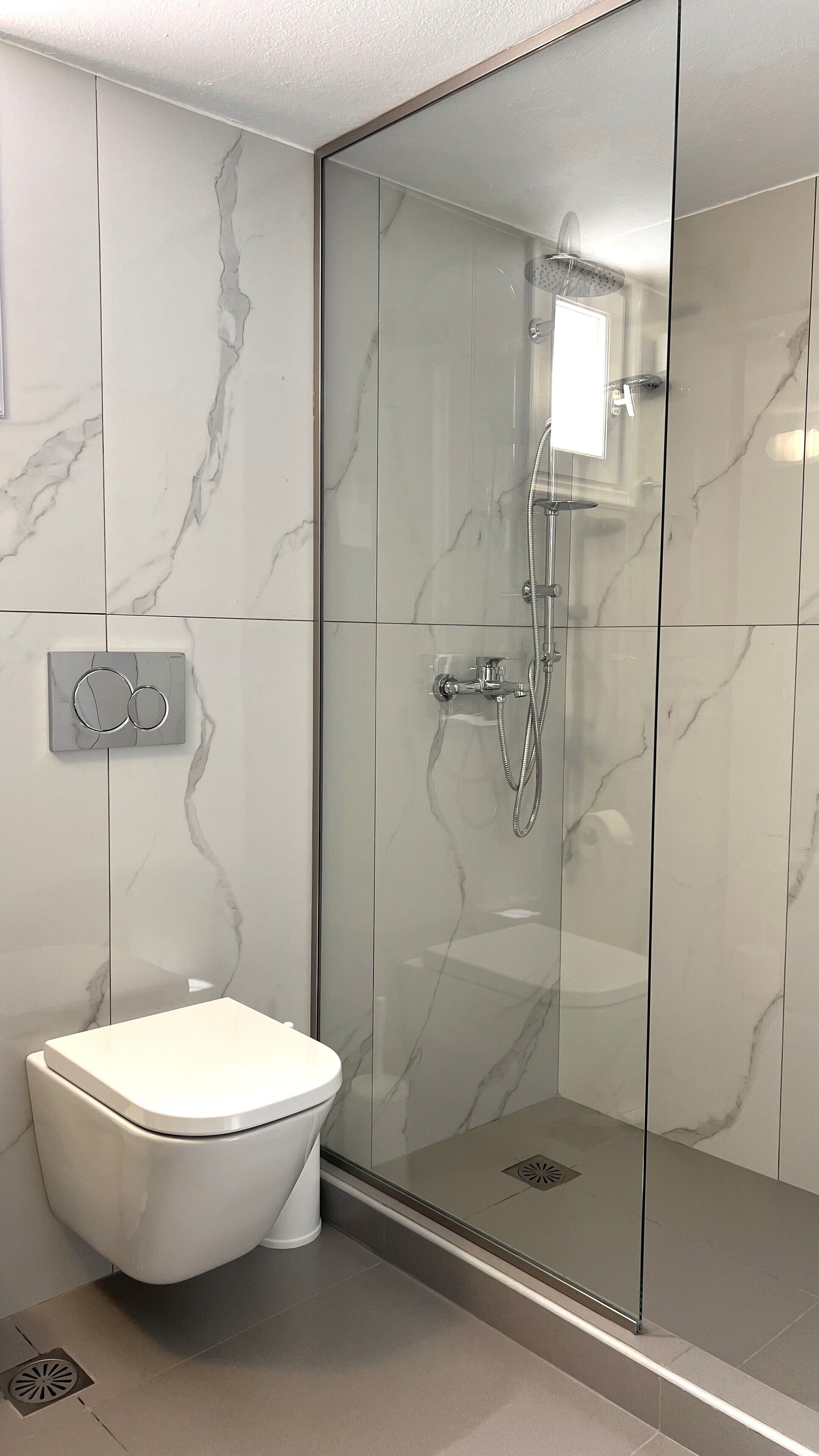 A modern bathroom with a glass-enclosed shower, a toilet, and a marble backsplash.