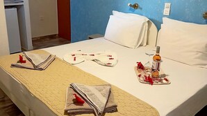 Habitación de hotel con cama, una mesita con una botella y vasos, y una toalla sobre la cama.