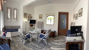Una sala de estar acogedora con un sofá, una mesa de comedor, sillas, un televisor y un ordenador sobre un escritorio.