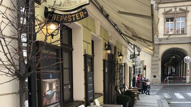 A restaurant with outdoor seating, a sign for 'Staropramen', and a view of a historic building in the background. - Hotel U Schnellu (Prague)