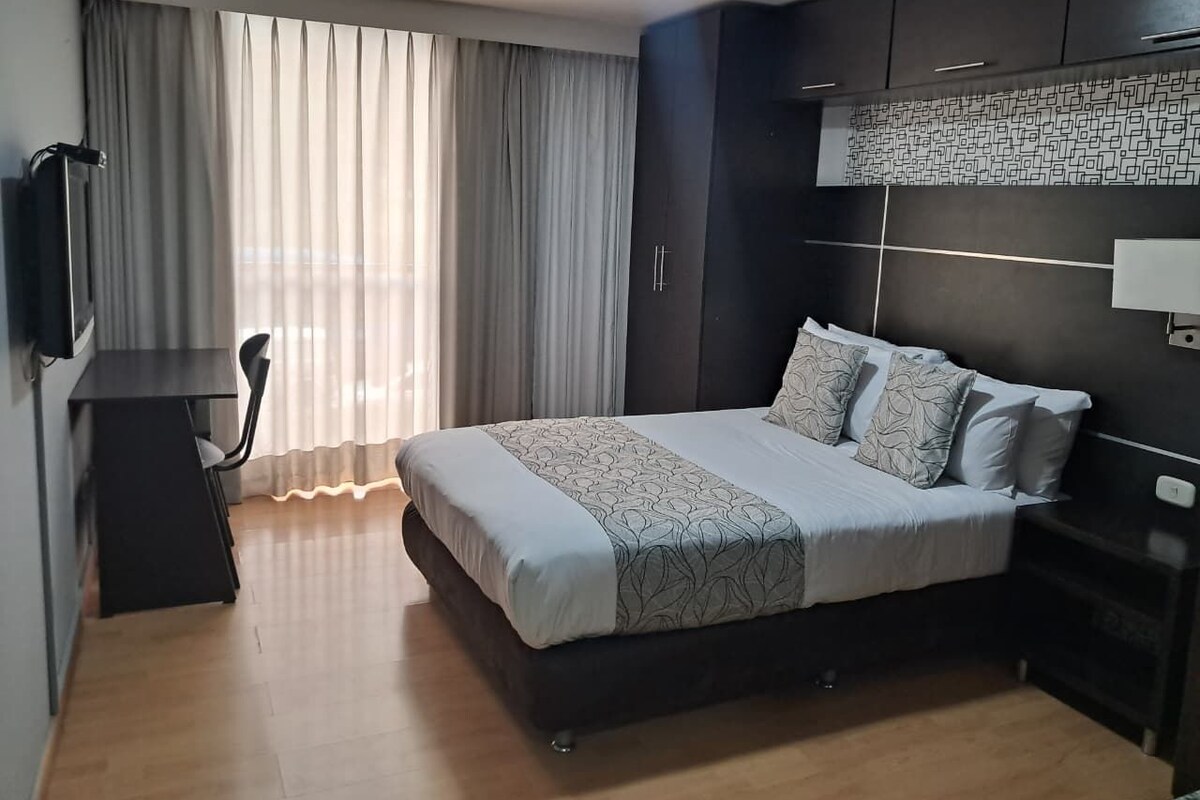 A modern hotel room with a bed, a desk, and a TV.