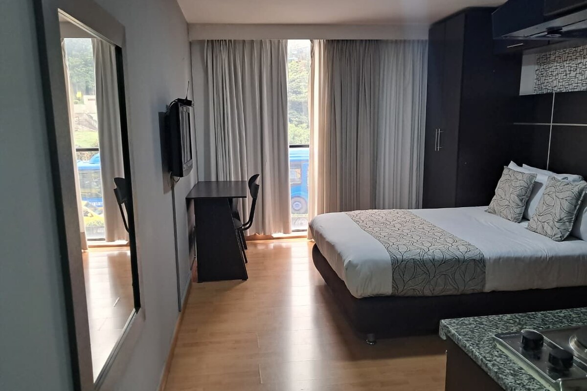 A bedroom with a bed, a desk, a TV, and a view of the outdoors.