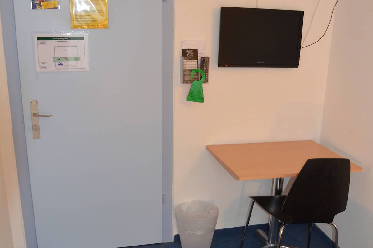A room with a bed, a desk, a chair, a TV, and a door.