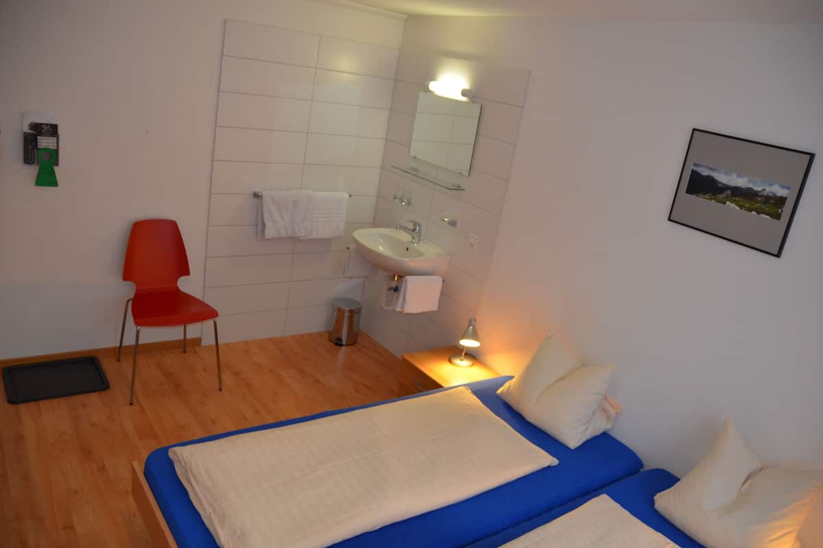 A hotel room with a bed, a chair, a sink, and a mirror.