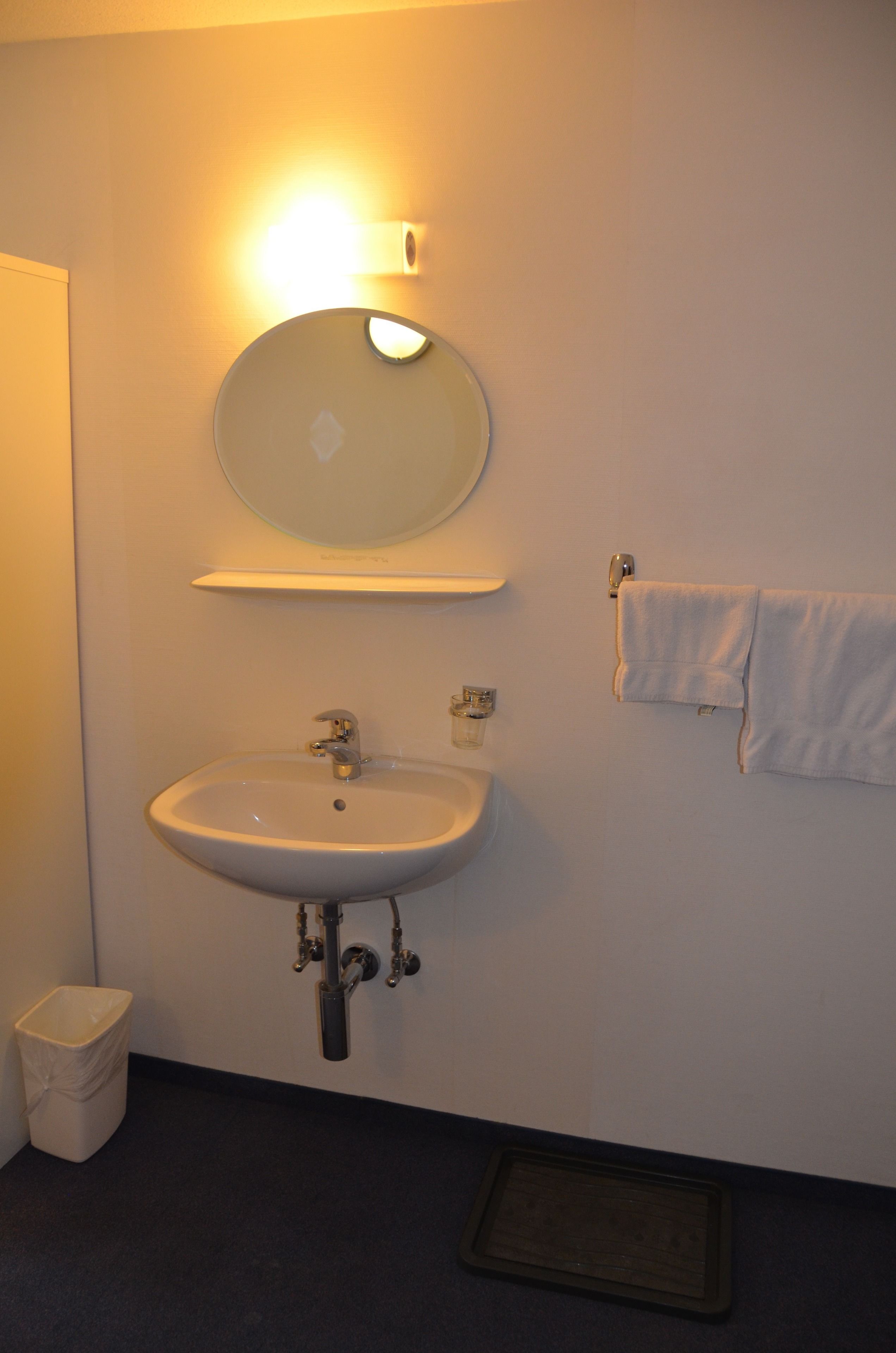 Ein Badezimmer mit Waschbecken, Spiegel, Handtuchhalter und Mülleimer.