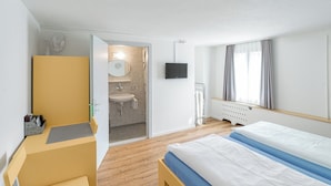 A hotel room with a bed, a desk, a chair, a bathroom with a sink and mirror, and a TV on the wall.