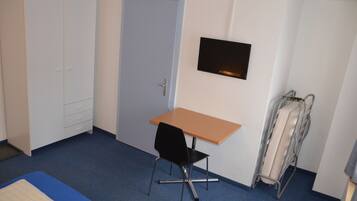 A small room with a single bed, a desk, a chair, a wardrobe, and a TV mounted on the wall.