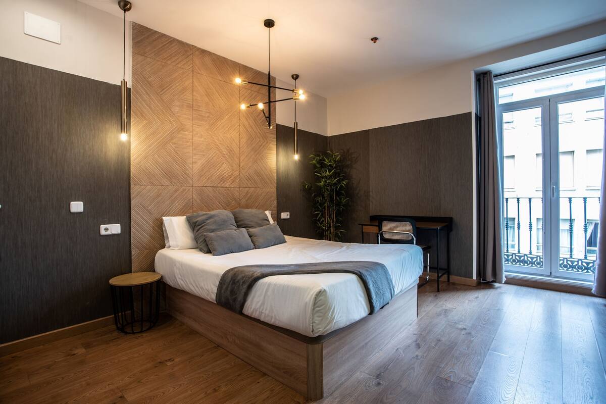 A modern bedroom with a large bed, a desk, a chair, and a view of the outside.