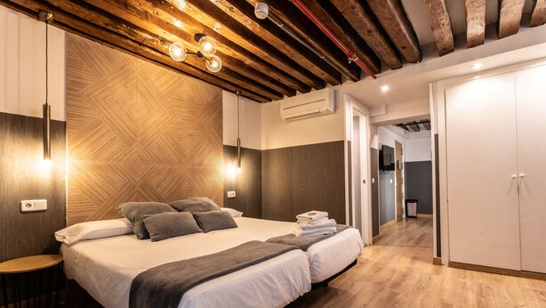 A modern bedroom with a large bed, wooden ceiling beams, and a built-in wardrobe. - Suites You Zinc (Madrid)