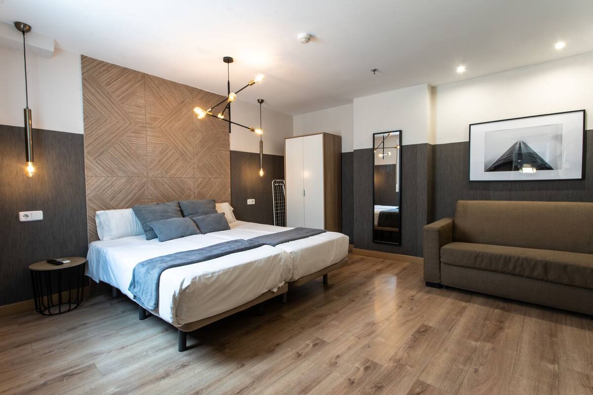 A modern bedroom with a large bed, a sofa, and a mirror.