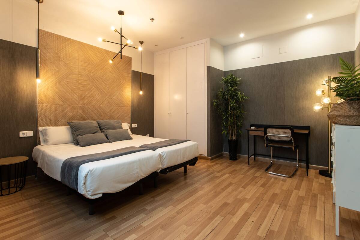 A modern bedroom with a large bed, a desk, and a potted plant.
