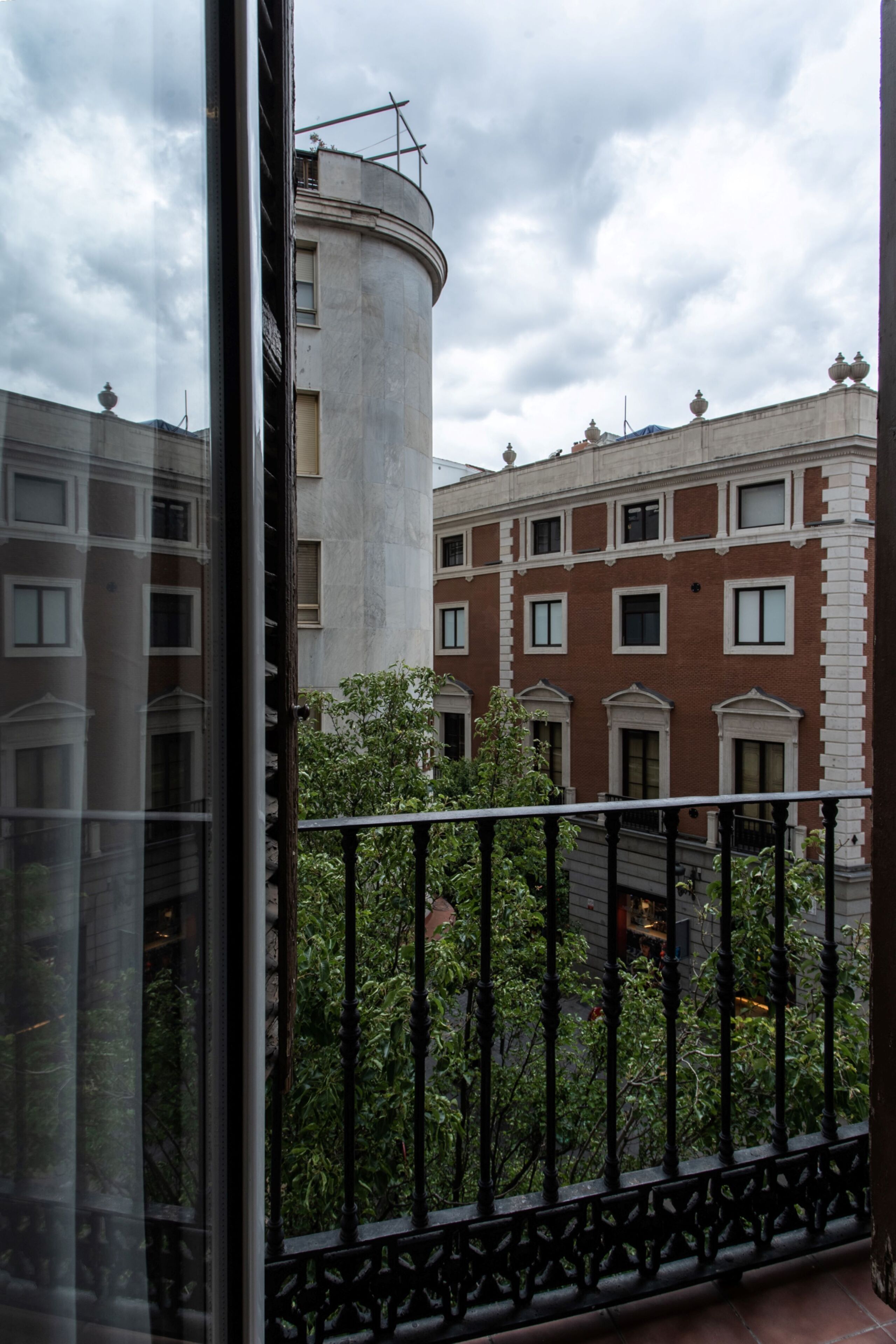 A view from a balcony with a metal railing, overlooking a building with a cylindrical structure and a red facade with white trim.